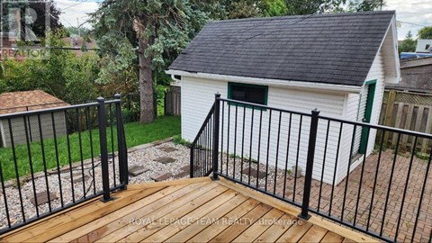 A small white building with a black roof and a green door is surrounded by a black metal fence.
