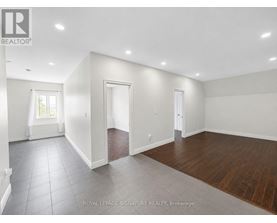 A spacious room with white walls and wooden flooring.