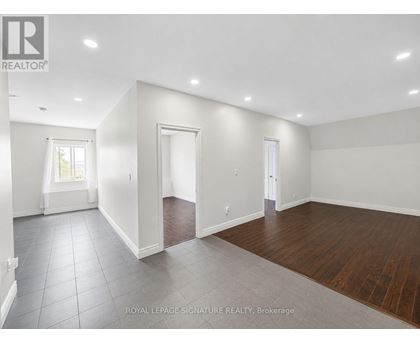 A spacious room with white walls and wooden flooring.