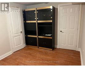 A large black wardrobe with a mirrored door is in a room with a white door and wooden flooring.