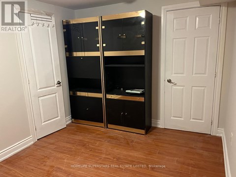 A large black wardrobe with a mirrored door is in a room with a white door and wooden flooring.