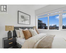 A bedroom with a large bed, a nightstand with a lamp, and a framed picture on the wall.