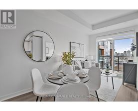 A dining room with a white table and chairs, a round mirror, and a view of the city.