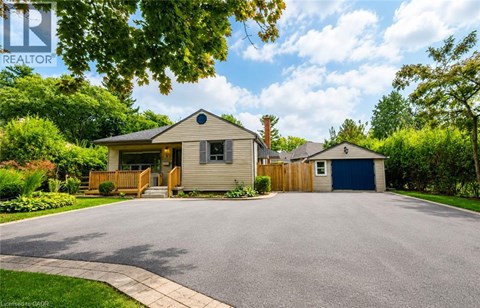 A house with a grey roof and a blue garage door is surrounded by greenery.