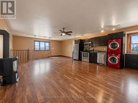 A wood floor in a large empty room with a wood stove and a washer and dryer.