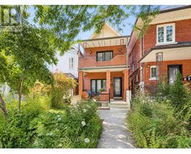 A red brick house with a white door and windows is surrounded by greenery.