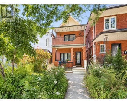 A red brick house with a white door and windows is surrounded by greenery.