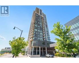 A tall building with many windows is surrounded by trees and has a clear blue sky in the background.