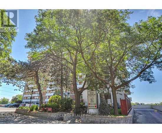 A real estate sign is in front of a building with trees.