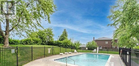 A pool surrounded by a black fence with trees in the background.