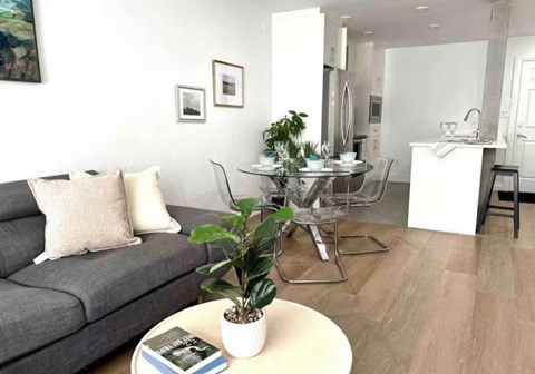 A living room with a grey couch, a coffee table, and a dining table set up.
