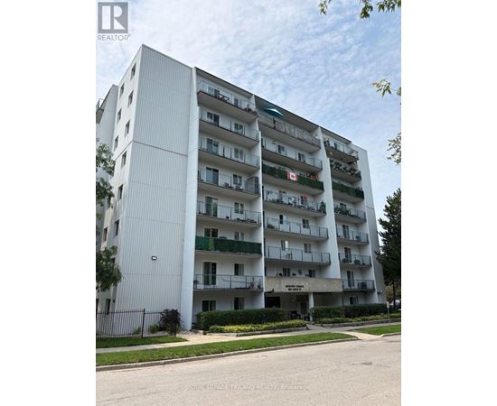 A tall white apartment building with balconies and a black fence in front.
