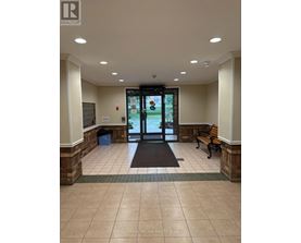 The image shows the front entrance of a building with a glass door and a bench on the right side.