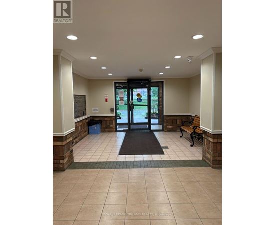 The image shows the front entrance of a building with a glass door and a bench on the right side.