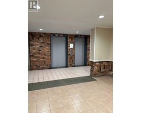 Two elevators in a hallway with a brick wall on one side and a white wall on the other.