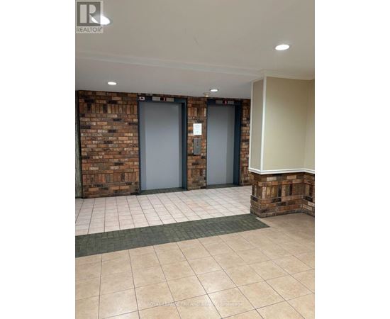 Two elevators in a hallway with a brick wall on one side and a white wall on the other.
