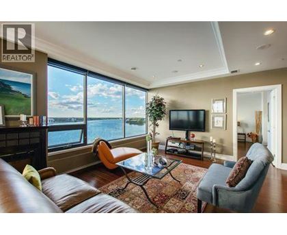 A living room with a brown leather couch, a glass coffee table, and a large window overlooking a body of water.