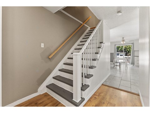 A staircase with a wooden handrail and white balusters leads to a dining area.