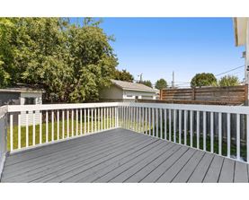 A wooden deck with a white railing and a backdrop of trees and houses.