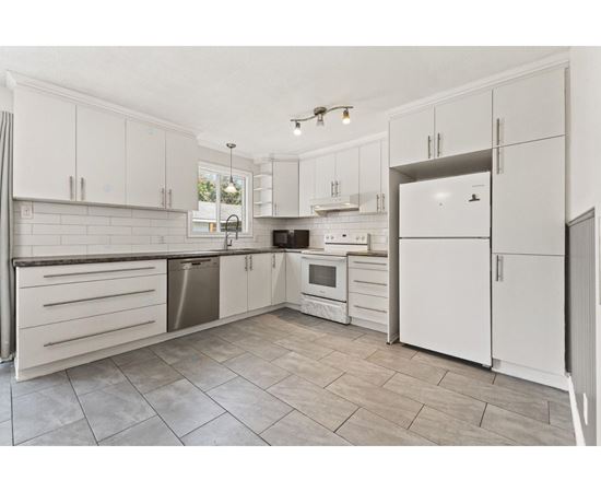 A kitchen with white cabinets and tile flooring.
