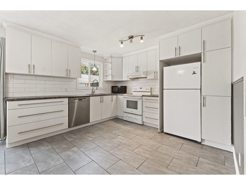 A kitchen with white cabinets and tile flooring.