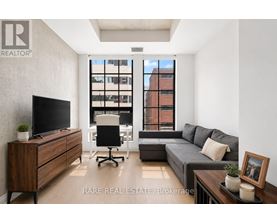 A living room with a grey couch, a wooden cabinet, a black office chair, and a television.