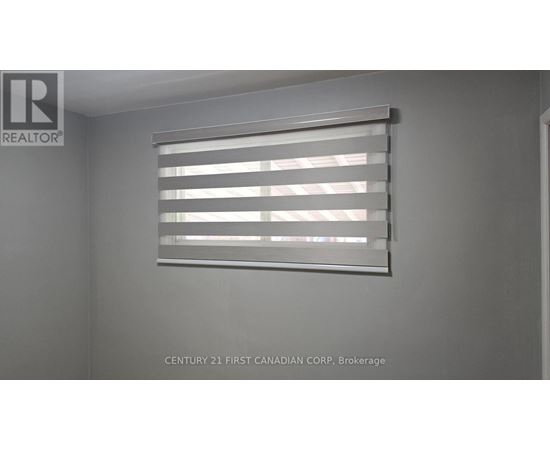 A window with blinds in a room with a realtor sign.