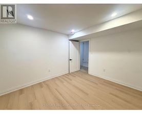 A room with a wooden floor and white walls, with a doorway leading to another room.