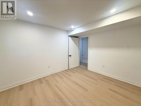 A room with a wooden floor and white walls, with a doorway leading to another room.