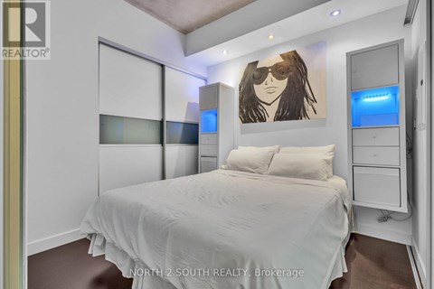 A bedroom with a bed, a dresser, and a painting of a woman with sunglasses on the wall.