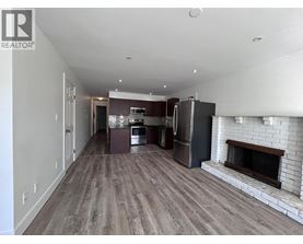A large, empty living room with a fireplace and a kitchen area in the background.