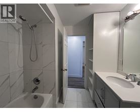 A bathroom with a white tub and sink, a shower with a hose, and a door leading to another room.