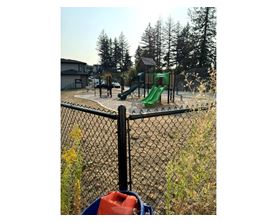 A playground with a green slide and a black fence.