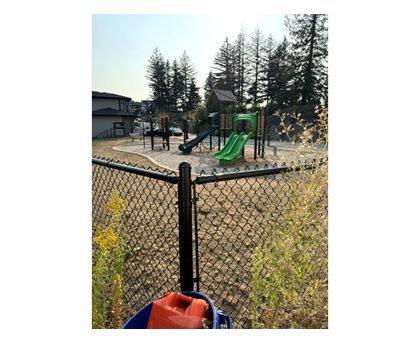 A playground with a green slide and a black fence.