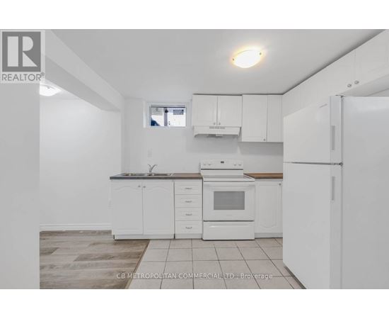 A white kitchen with a refrigerator, sink, and oven.