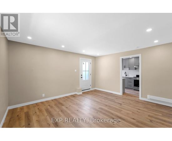A room with wooden flooring and a doorway leading to a kitchen.
