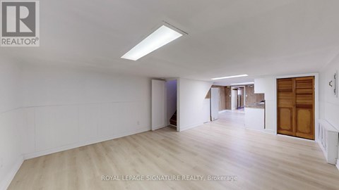 A spacious room with wooden flooring and white walls, with a door on the right side.