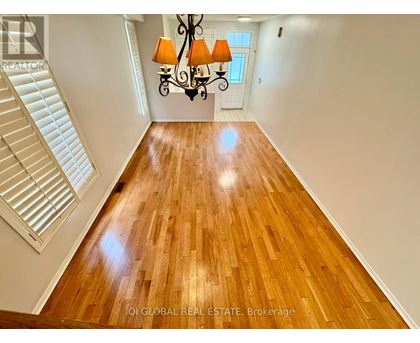 A well-lit, spacious room with wooden flooring and a staircase on the left side.