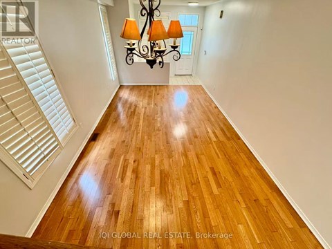 A well-lit, spacious room with wooden flooring and a staircase on the left side.