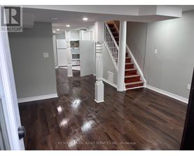 A hallway with a staircase and a kitchen in the background.