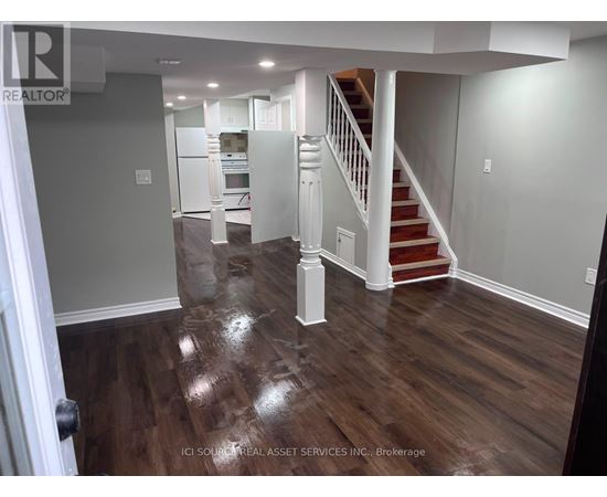 A hallway with a staircase and a kitchen in the background.