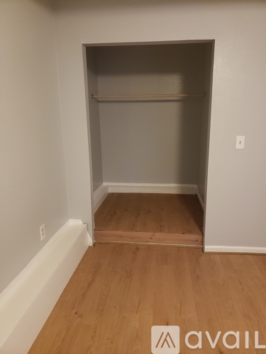 A room with a wooden floor and a white wall with a shelf in the corner.