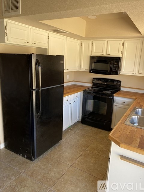 A black refrigerator in a kitchen with white cabinets.