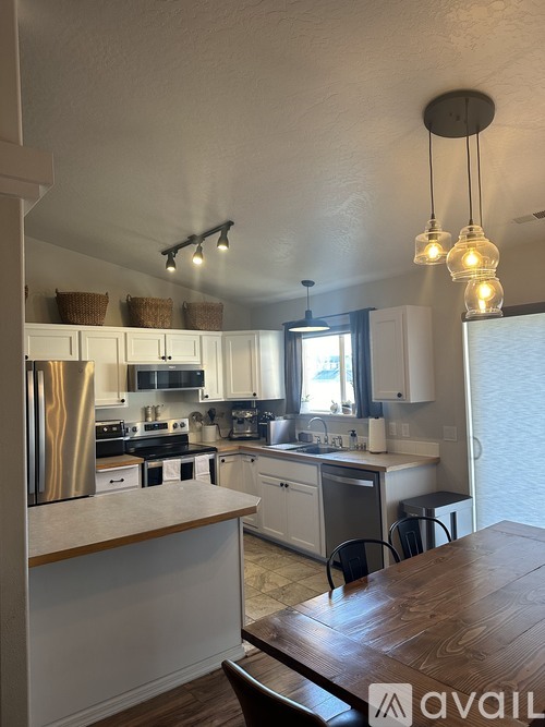 A kitchen with a table and chairs in the foreground and a refrigerator, microwave, oven, and sink in the background.