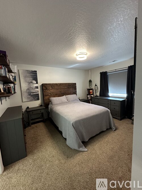 A bedroom with a bed, nightstand, and a window with black curtains.