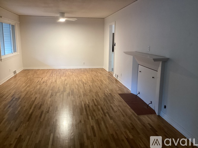 A room with wooden flooring and white walls, with a door on the right and a window on the left.