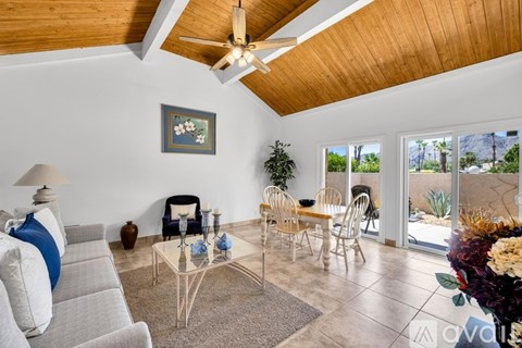 A living room with a grey sofa, a glass coffee table, a ceiling fan, and a painting on the wall.
