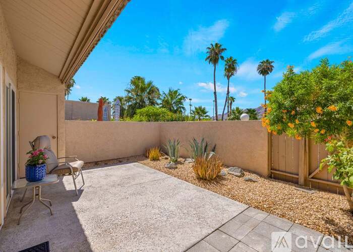 A patio with a table and chairs is surrounded by a wall and has a view of palm trees.
