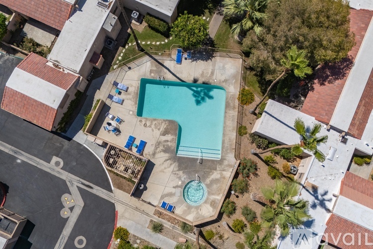 An aerial view of a swimming pool surrounded by a parking lot and palm trees.