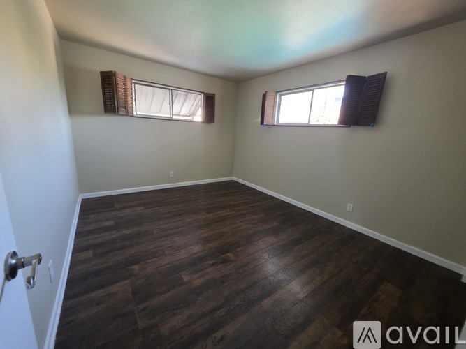A room with wooden flooring and two windows with blinds.